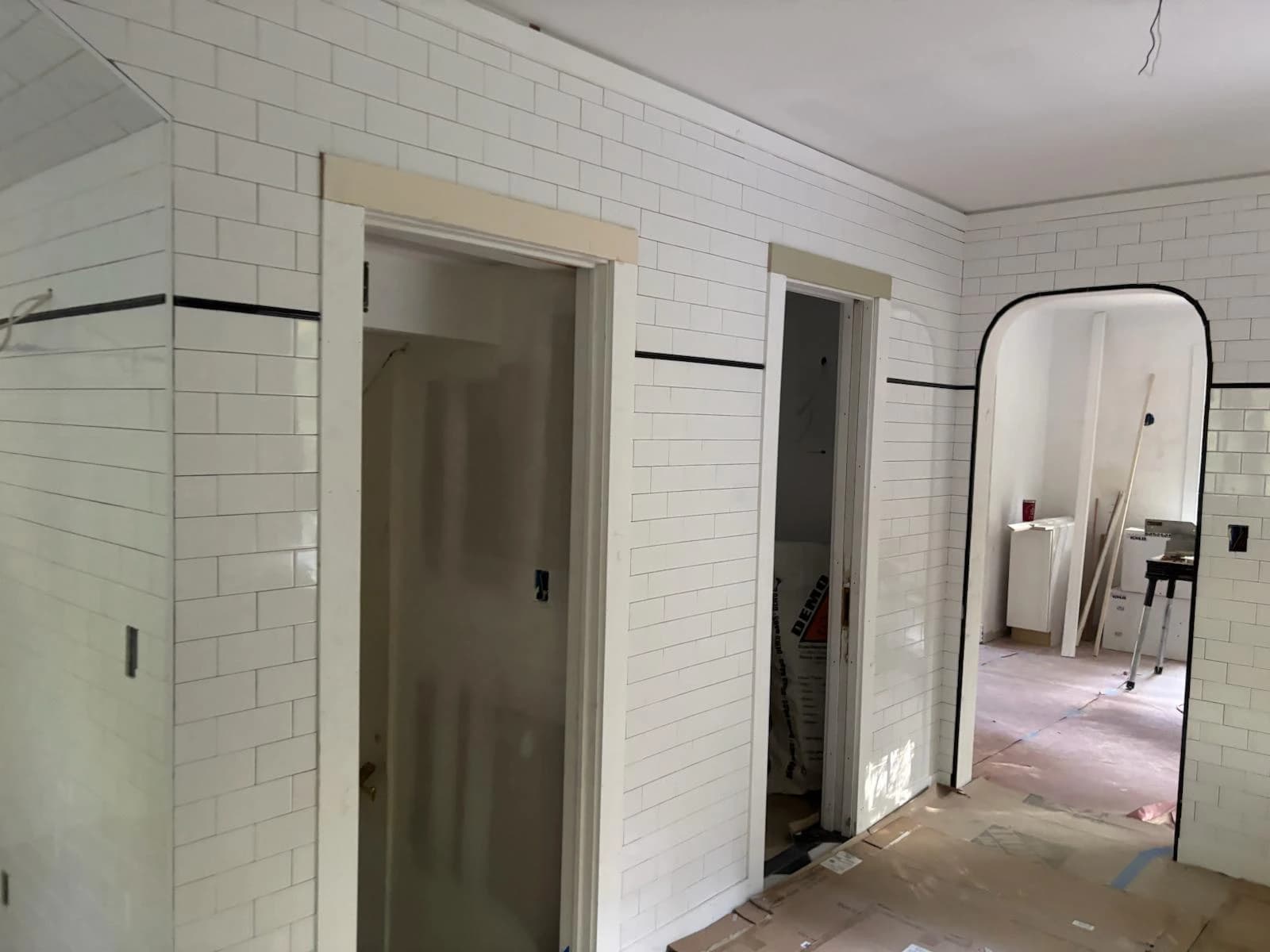 White subway-tiled bathroom mid-renovation with an arched doorway and a black accent stripe - Greater Homes Solutions LLC