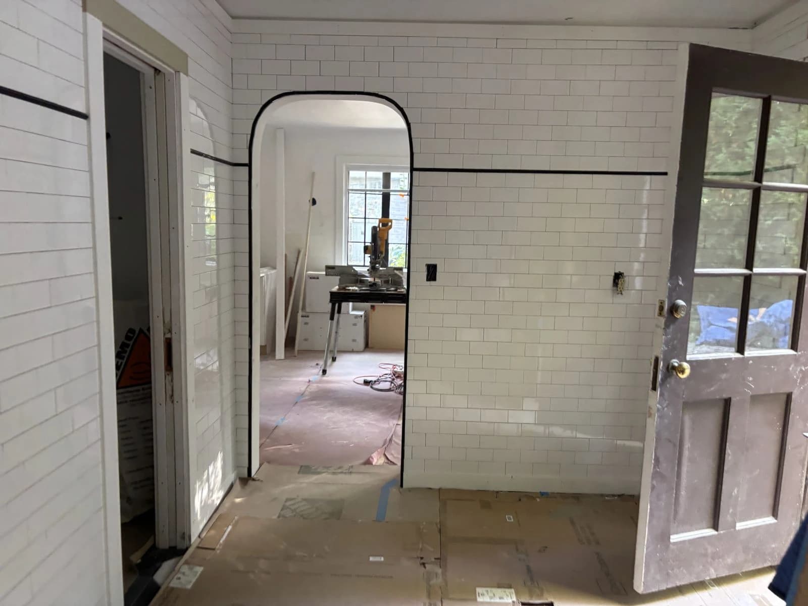 Subway-tiled room mid-renovation with an arched doorway and a black tile border stripe - Greater Homes Solutions LLC
