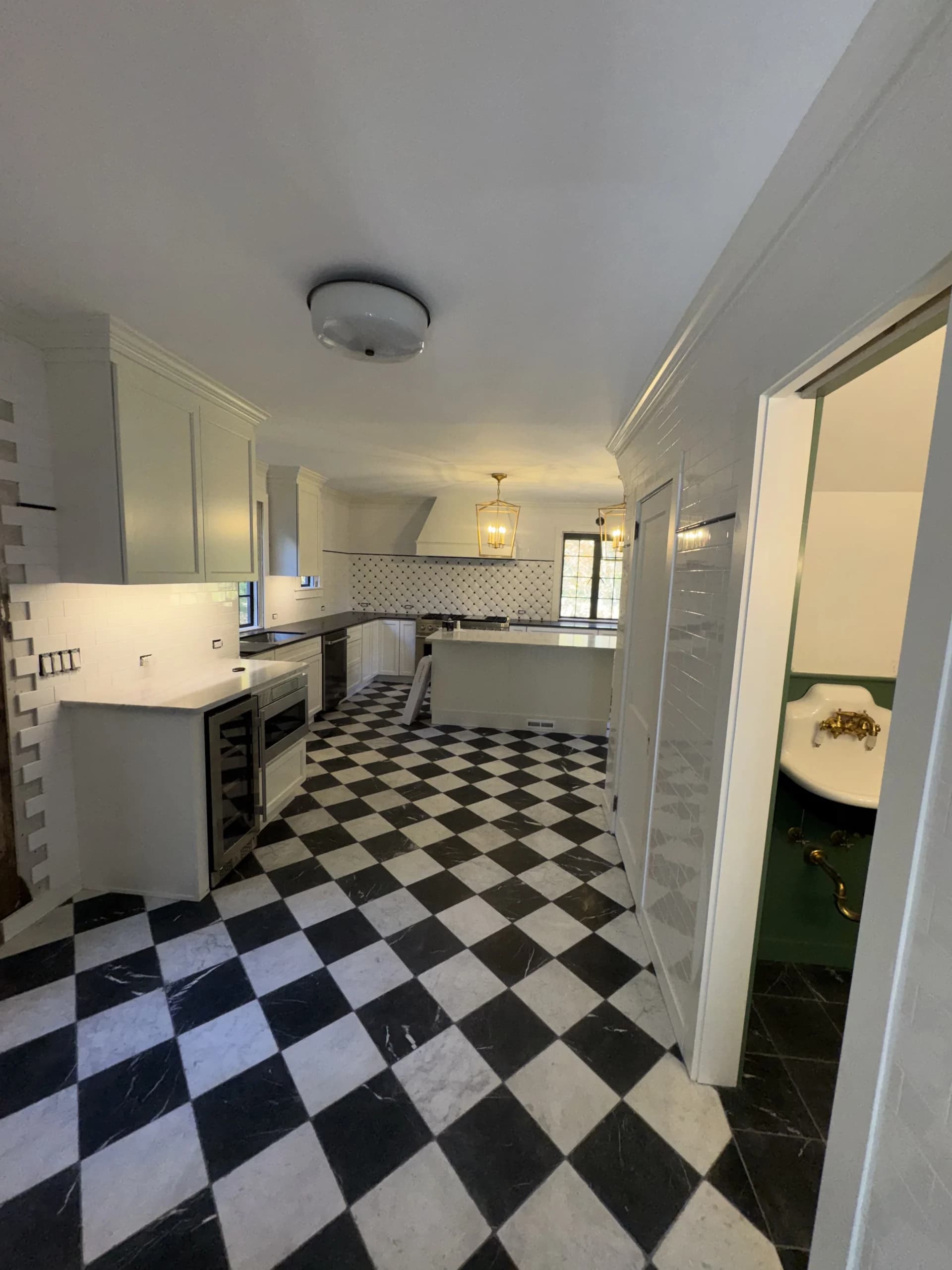 Hallway into a kitchen with a black and white checkered floor and white cabinets - home renovation by Greater Homes Solutions LLC