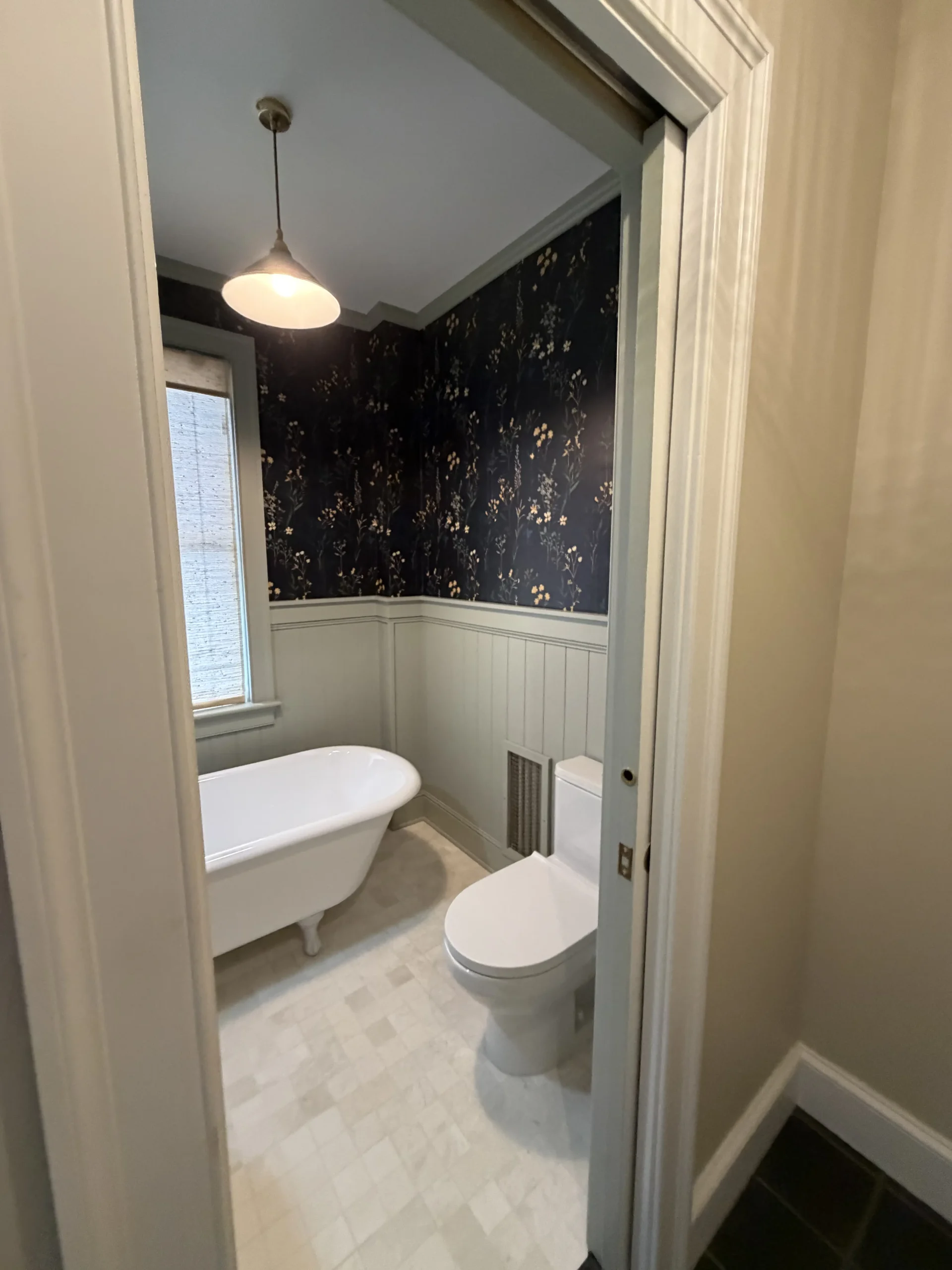 Powder room with dark wallpaper, wainscoting, a clawfoot tub and a pendant light - bathroom remodeling by Greater Homes Solutions LLC