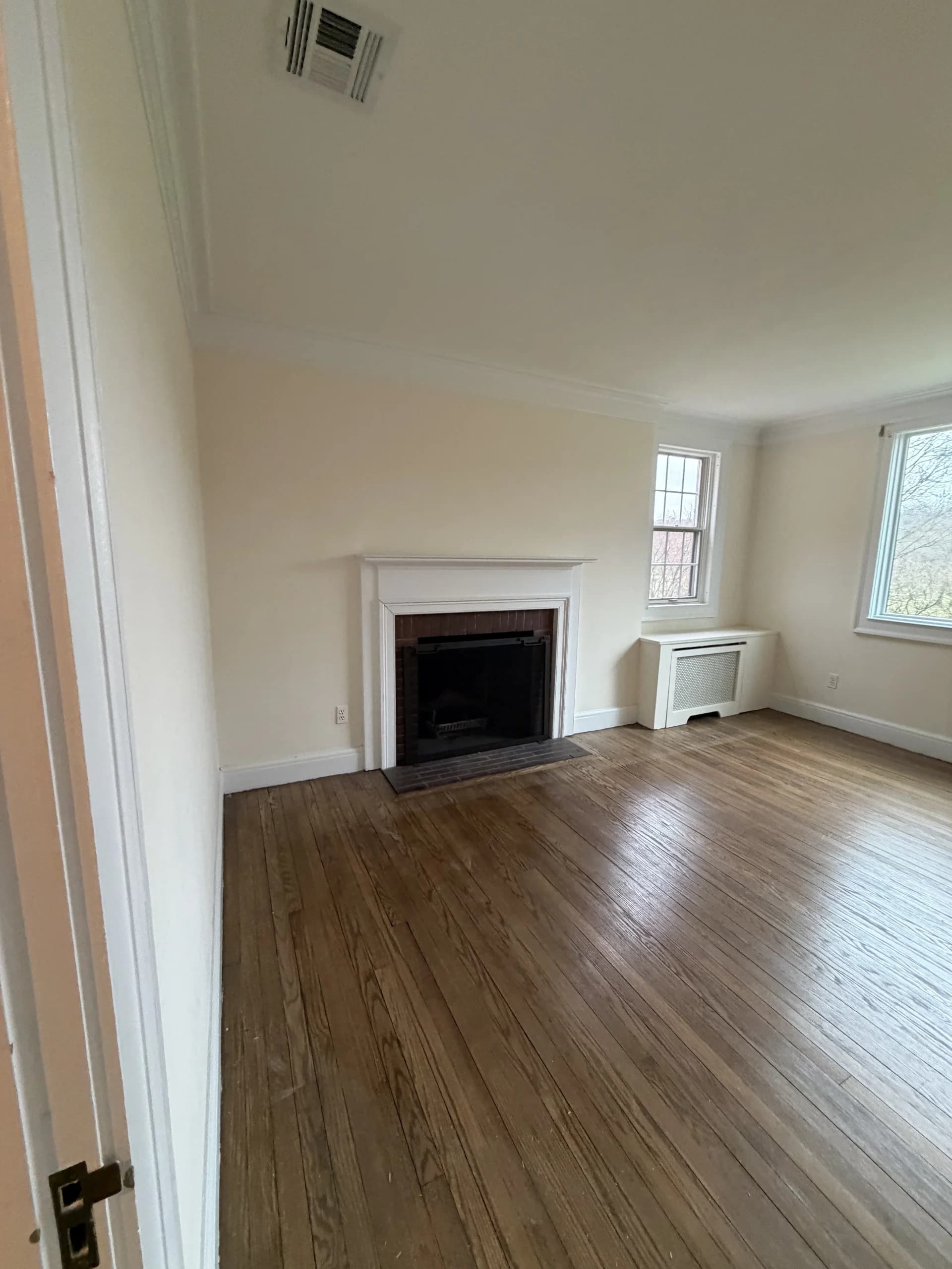 Empty room with refinished hardwood floors, a fireplace and freshly painted walls - interior renovation by Greater Homes Solutions LLC