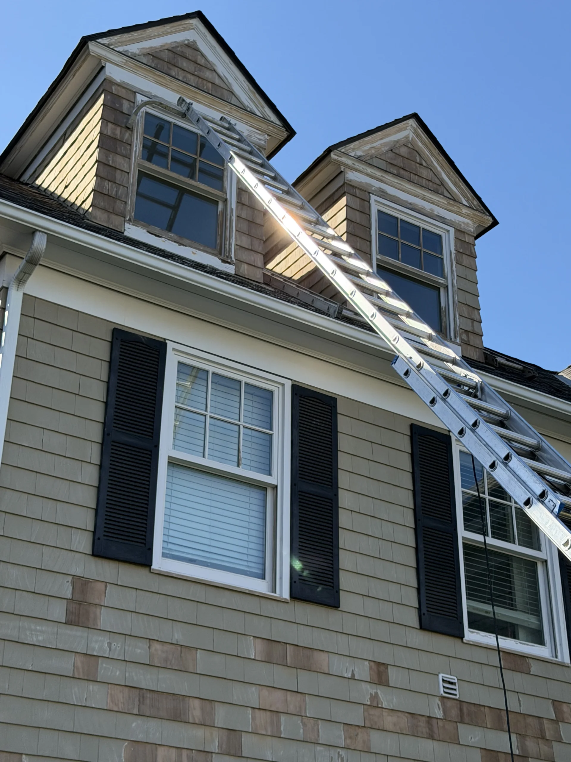 Ladder set against a shingled home with two dormer windows during exterior work by Greater Homes Solutions LLC