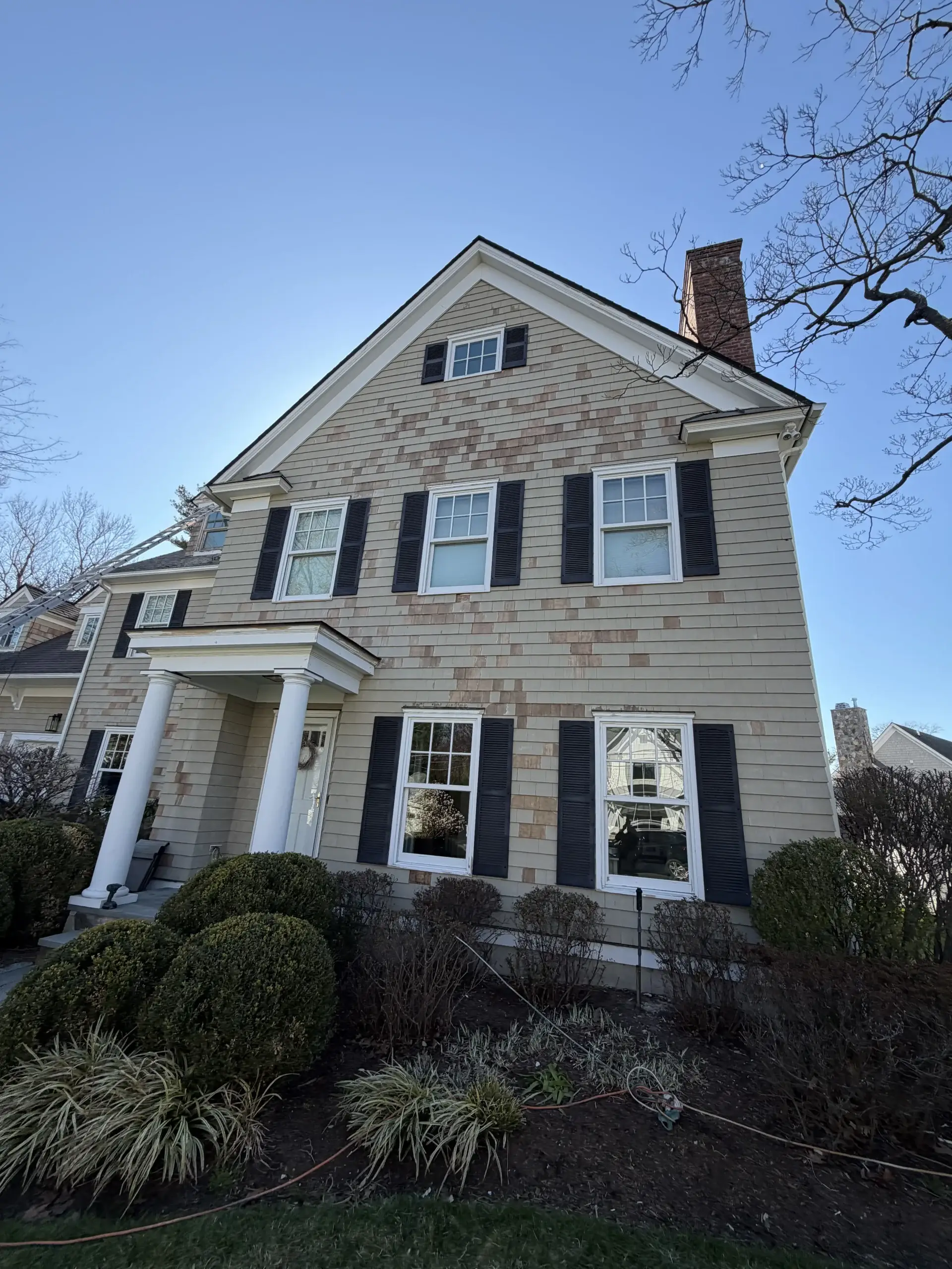 Two-story colonial home with black shutters, a front portico and a brick chimney - Greater Homes Solutions LLC
