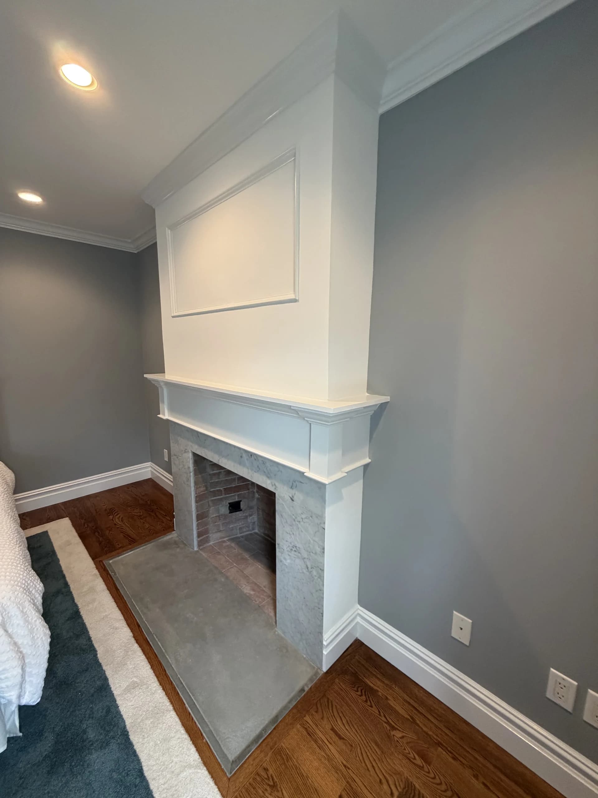 Fireplace with a white paneled mantel and marble surround beside a window in a grey bedroom - Greater Homes Solutions LLC