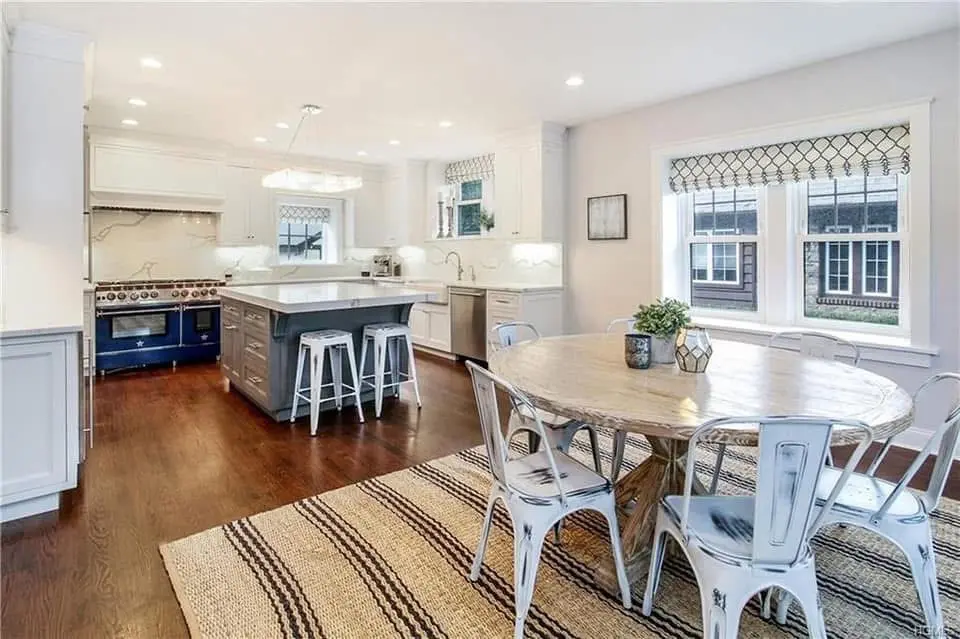 White kitchen with a navy island, bar stools and a round farmhouse dining table - kitchen remodeling by Greater Homes Solutions LLC