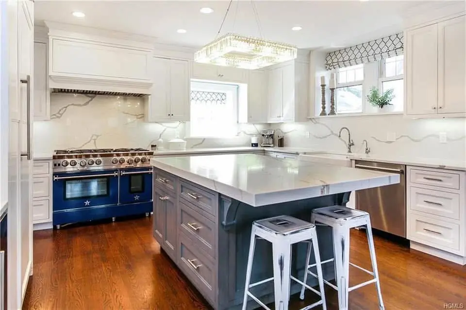 White kitchen with a marble waterfall island, a blue professional range and hardwood floors - kitchen remodeling by Greater Homes Solutions LLC