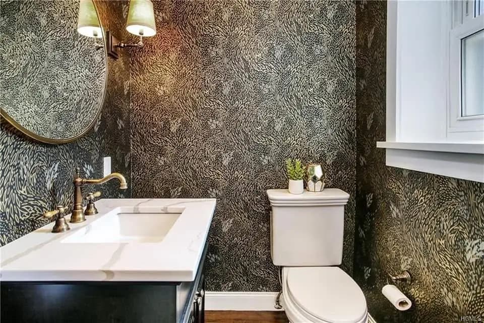 Powder room with patterned wallpaper, a marble-topped vanity and brass fixtures - bathroom remodeling by Greater Homes Solutions LLC