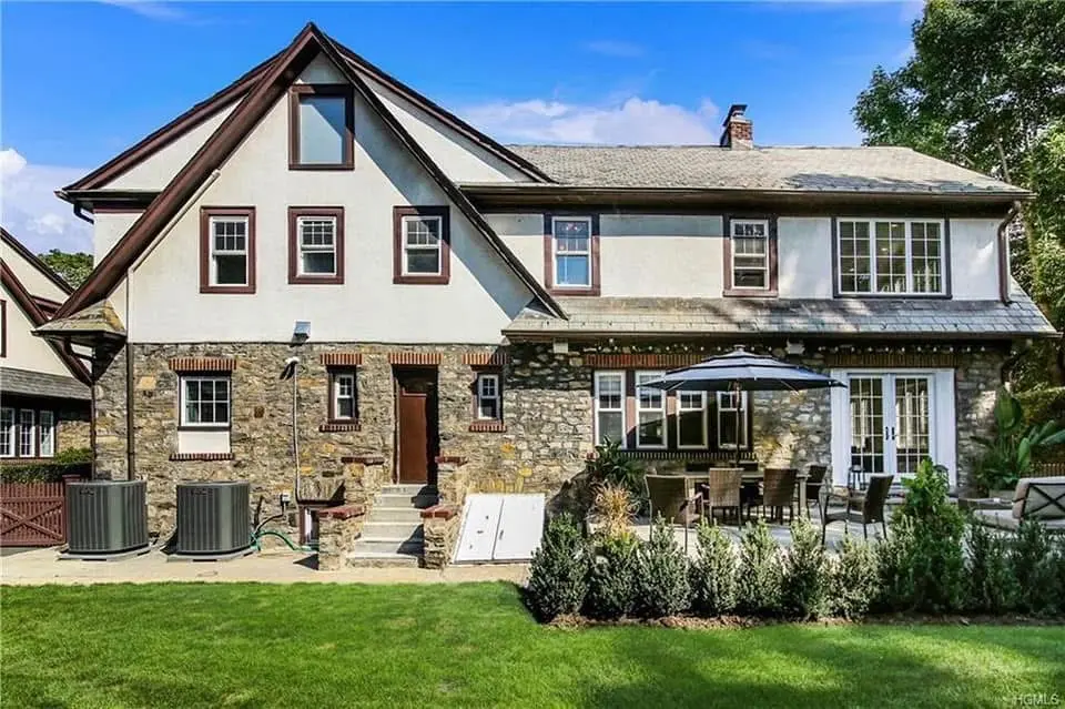 Stone and stucco Tudor-style home with a patio, outdoor seating and a landscaped lawn - Greater Homes Solutions LLC