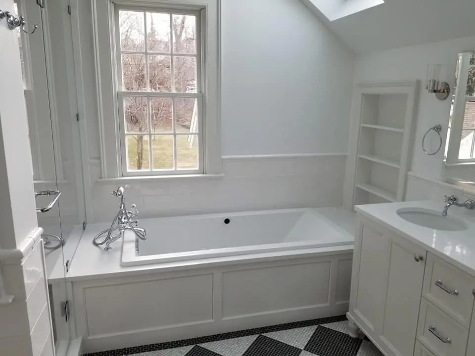 Bathroom with a built-in soaking tub under a window, white vanity and black and white tile floor - bathroom remodeling by Greater Homes Solutions LLC