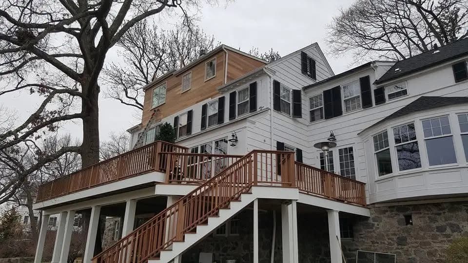 Elevated wood deck with stairs and railings on the back of a white colonial home - custom deck building by Greater Homes Solutions LLC