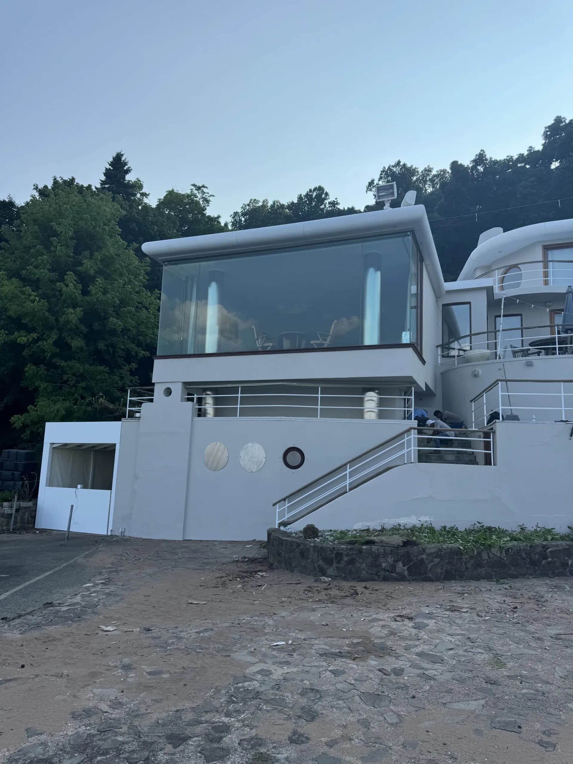 Modern white waterfront home with large windows, seen from the shore at dusk - Greater Homes Solutions LLC project site