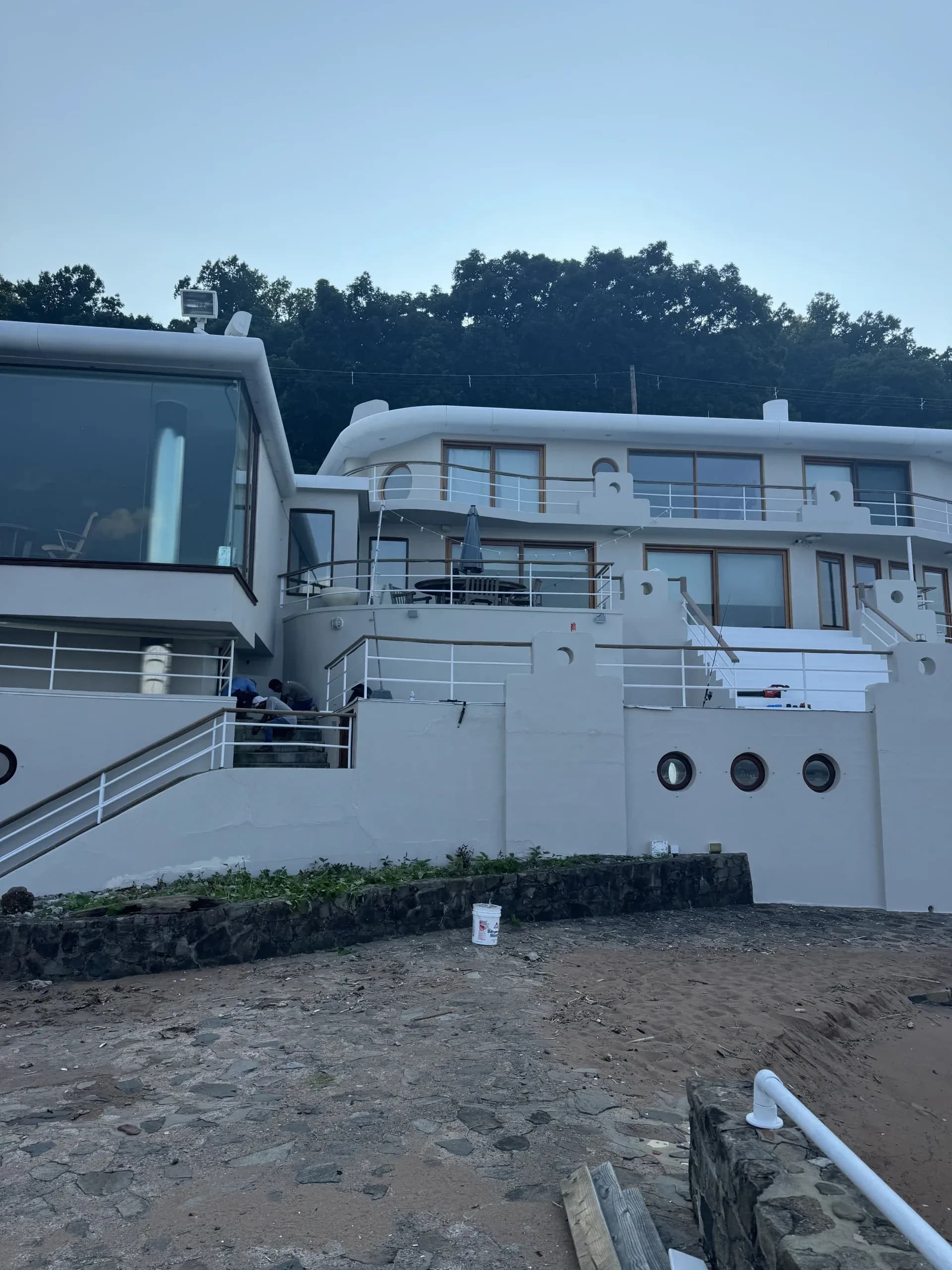 Modern white waterfront home with a rooftop deck and a sandy yard under construction - Greater Homes Solutions LLC