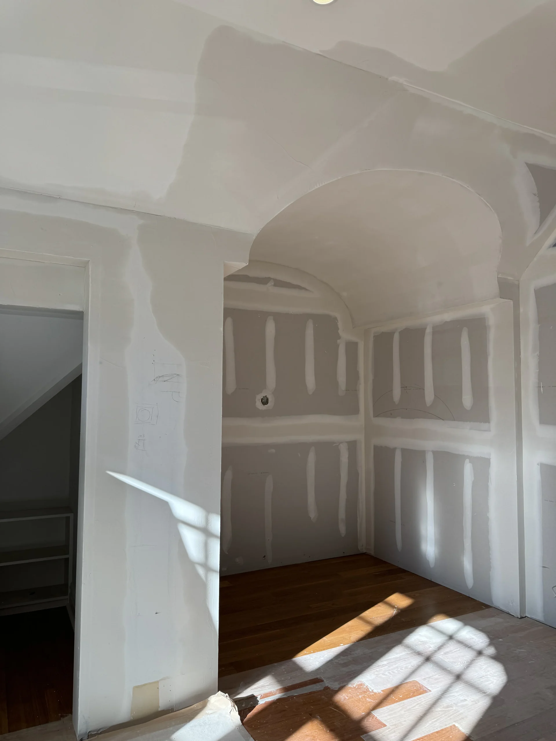Room mid-renovation with new drywall, an arched doorway and hardwood floors - interior renovation by Greater Homes Solutions LLC