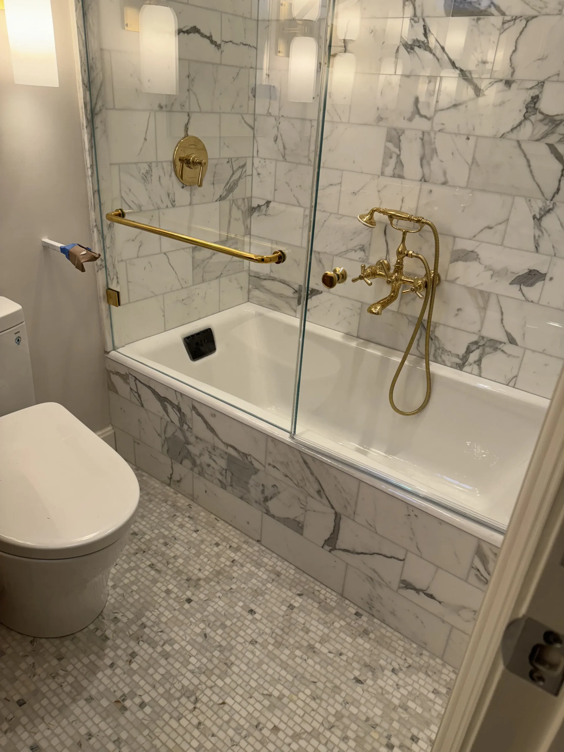 Bathroom with a marble-tiled tub and shower, brass fixtures and a mosaic tile floor - bathroom remodeling by Greater Homes Solutions LLC