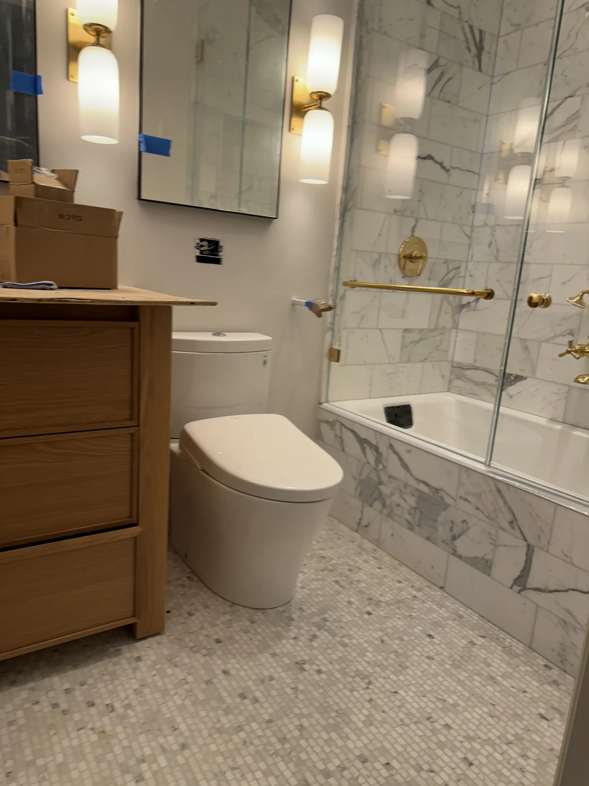 Bathroom mid-renovation with a new toilet, wood vanity, marble tile and brass tub fixtures - Greater Homes Solutions LLC