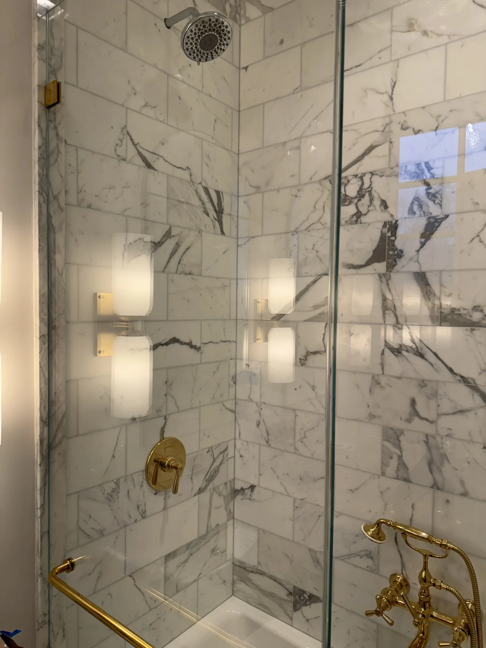 Walk-in shower with marble tile and brass fixtures behind a frameless glass door - bathroom remodeling by Greater Homes Solutions LLC
