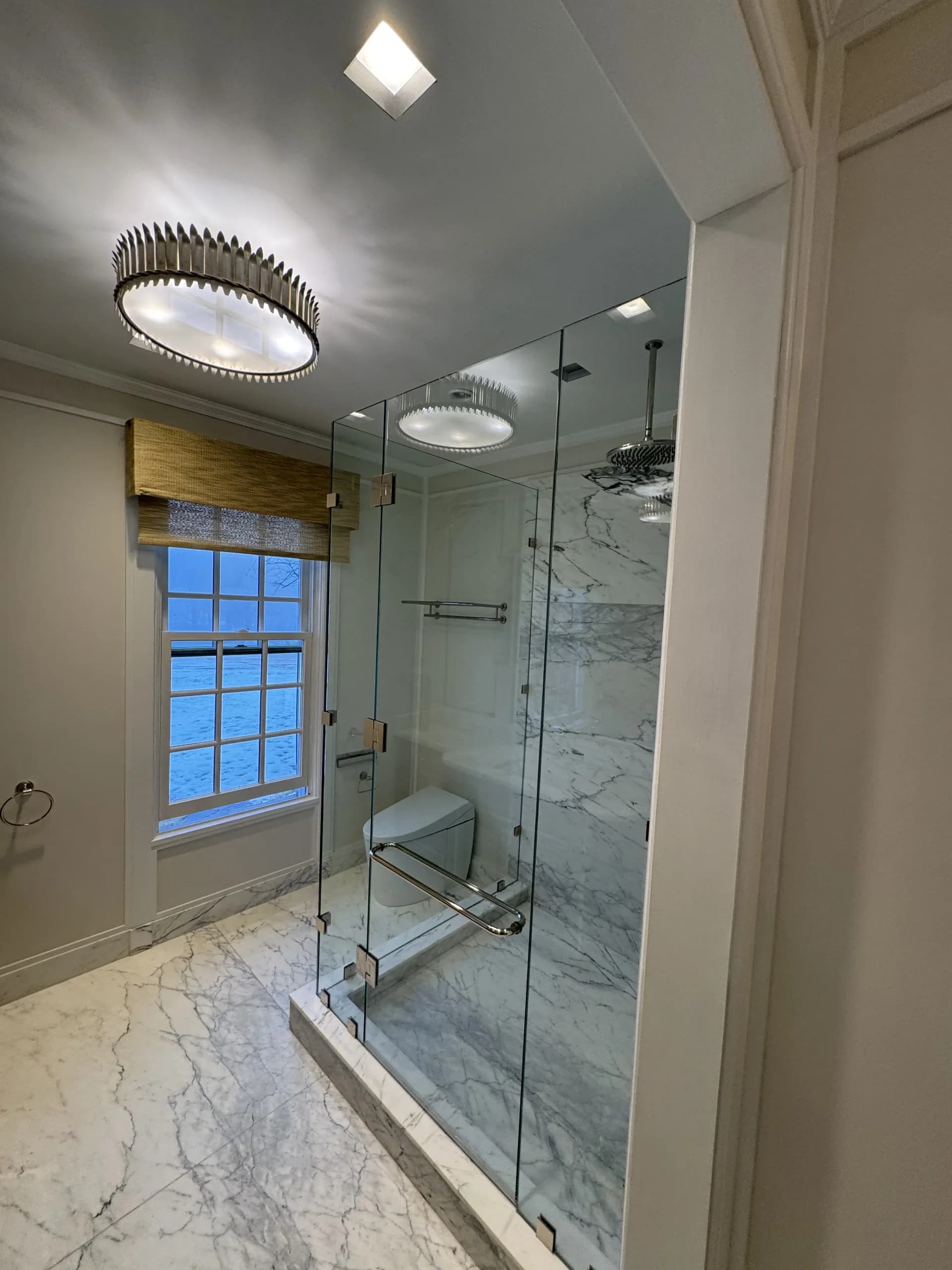 Frameless glass shower with marble tile beside a window and a double vanity - bathroom remodeling by Greater Homes Solutions LLC