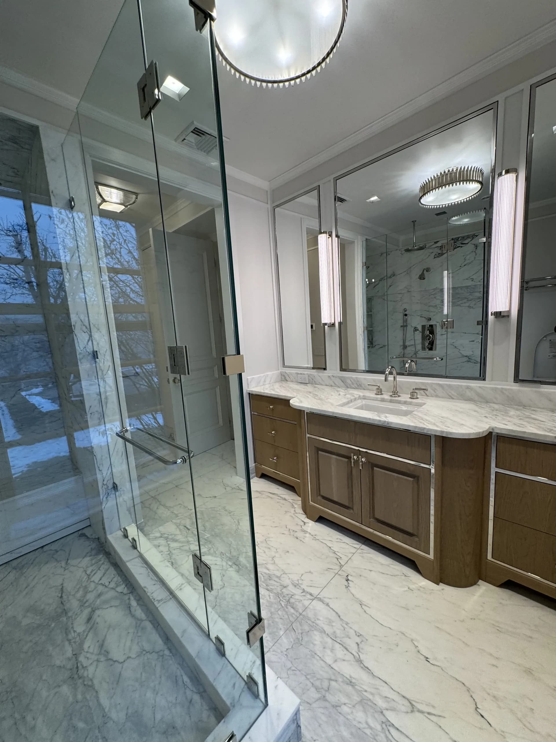 Marble bathroom with a glass shower enclosure and a double vanity with sconce lighting - bathroom remodeling by Greater Homes Solutions LLC