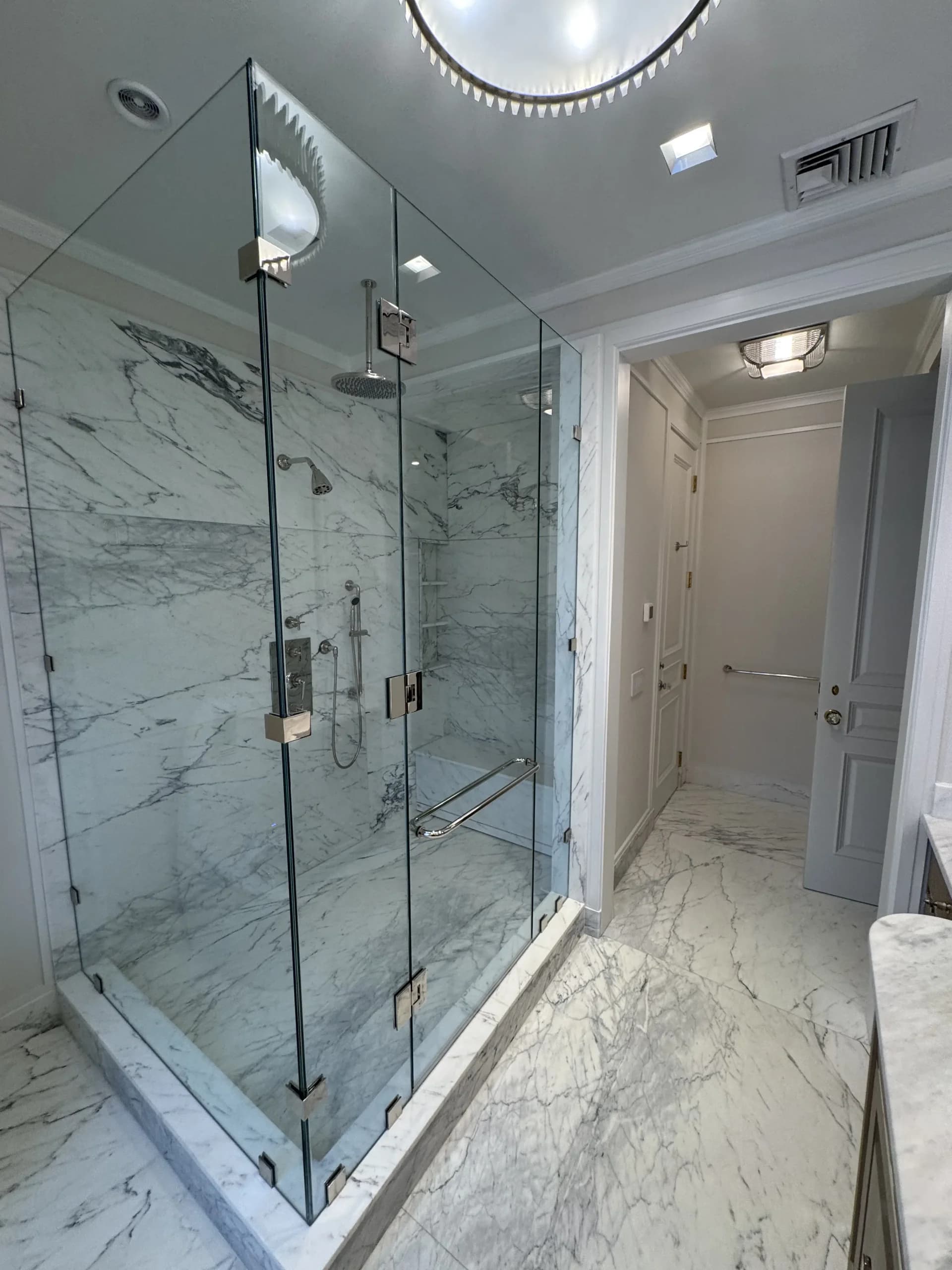 Frameless glass shower enclosure with marble tile and a built-in bench - bathroom remodeling by Greater Homes Solutions LLC