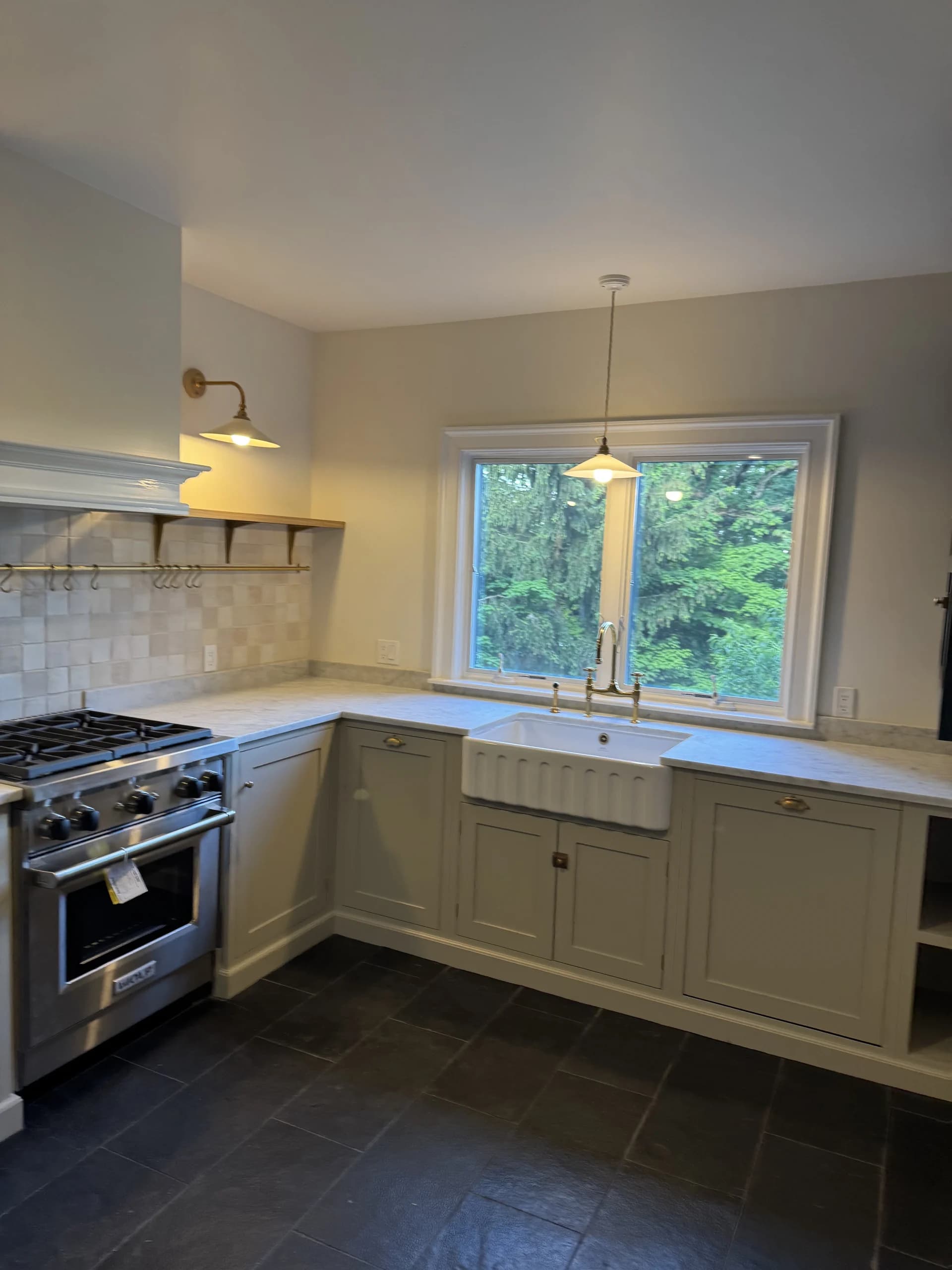 Kitchen with a farmhouse sink under a window, a stainless range and cream cabinets - kitchen remodeling by Greater Homes Solutions LLC