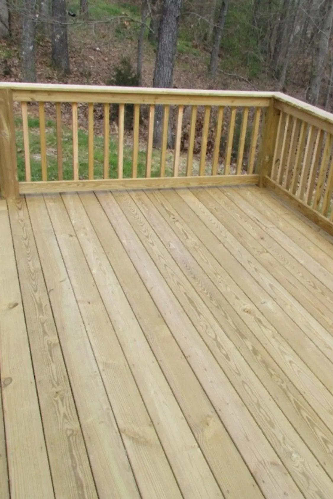 New pressure-treated wood deck with railings overlooking the woods - custom deck building by Greater Homes Solutions LLC