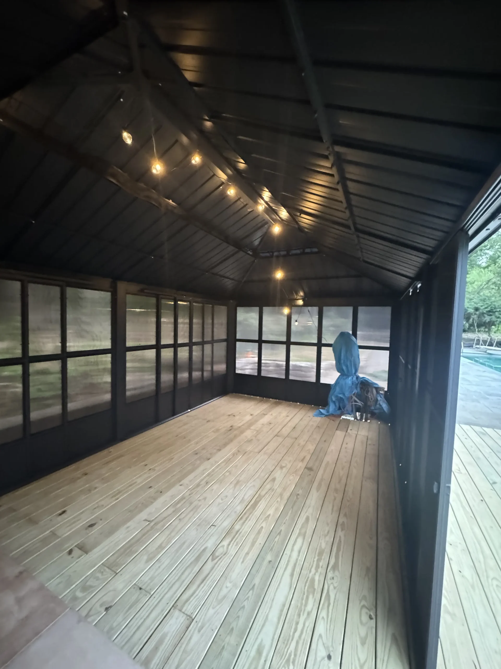 Inside a screened gazebo with a black ceiling, string lights and a wood deck floor - built by Greater Homes Solutions LLC