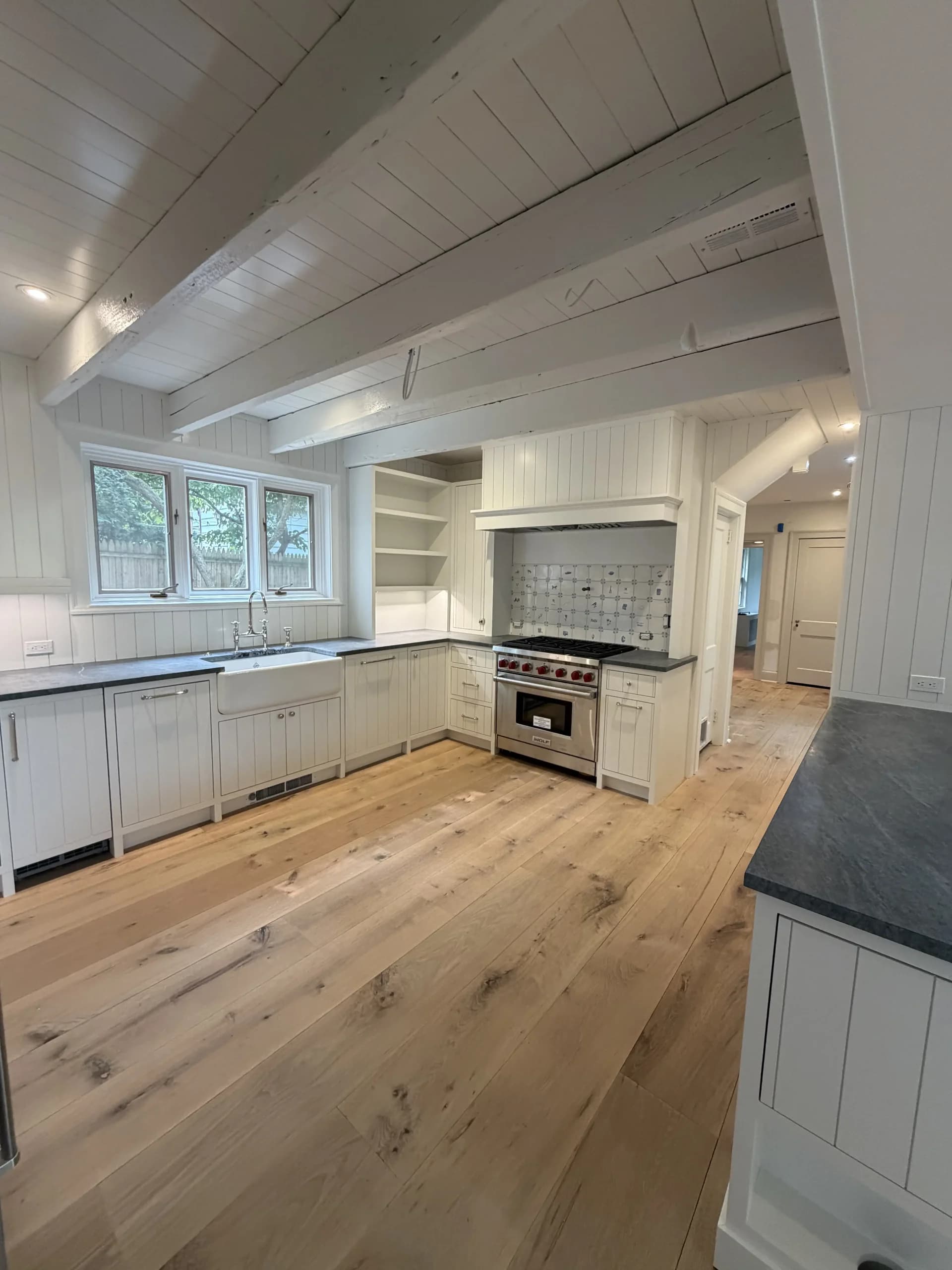 Renovated kitchen with a shiplap ceiling, white cabinets, a slate-topped island and wide plank oak floors - Greater Homes Solutions LLC
