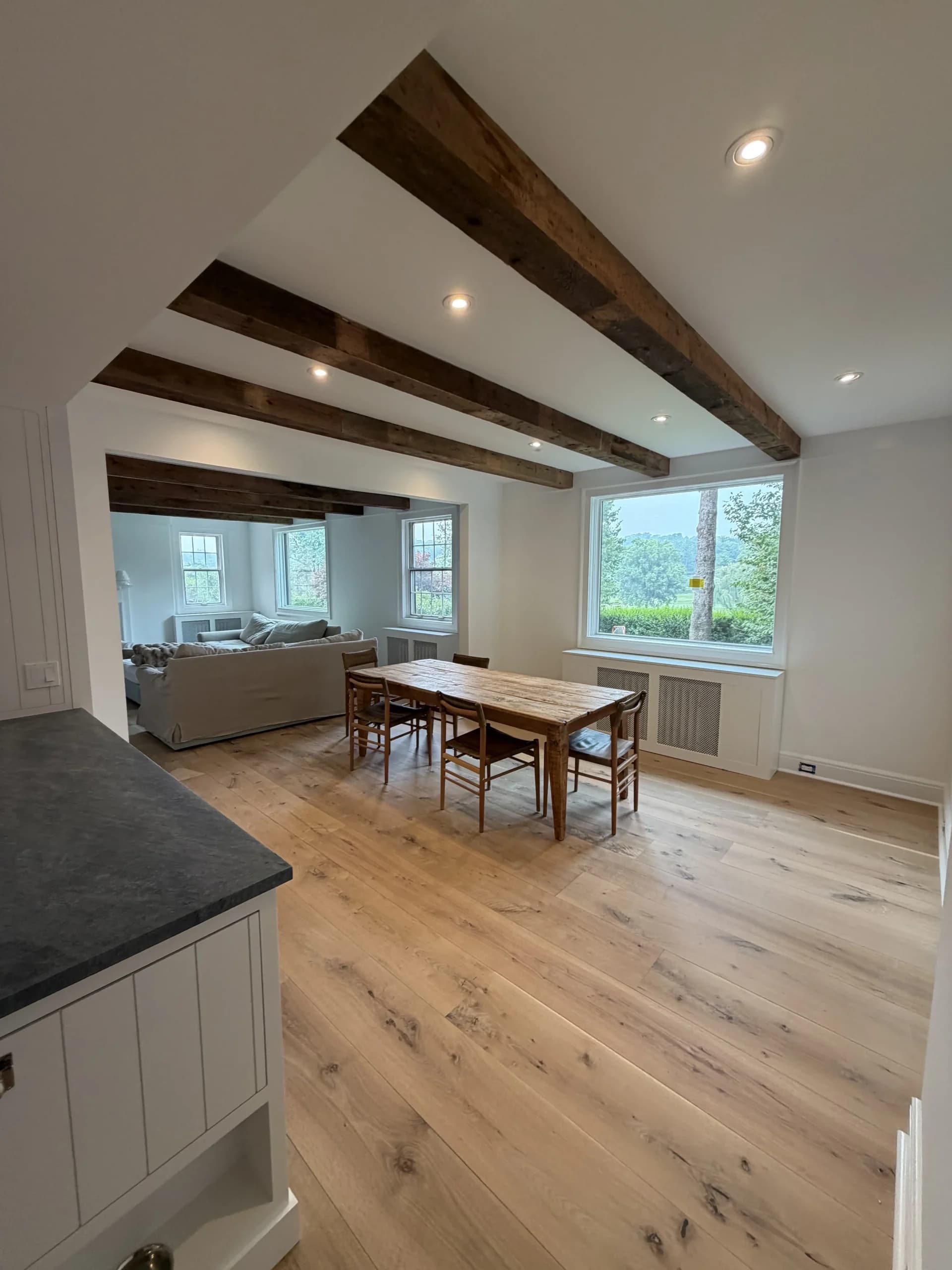 Kitchen island looking into a dining and living area with beamed ceilings and oak floors - home renovation by Greater Homes Solutions LLC