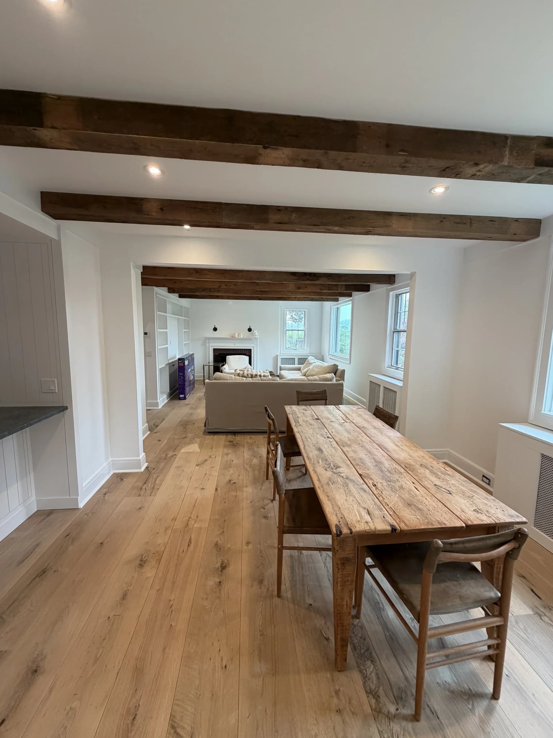 Open dining and living space with reclaimed wood beams and a long farmhouse table - home renovation by Greater Homes Solutions LLC