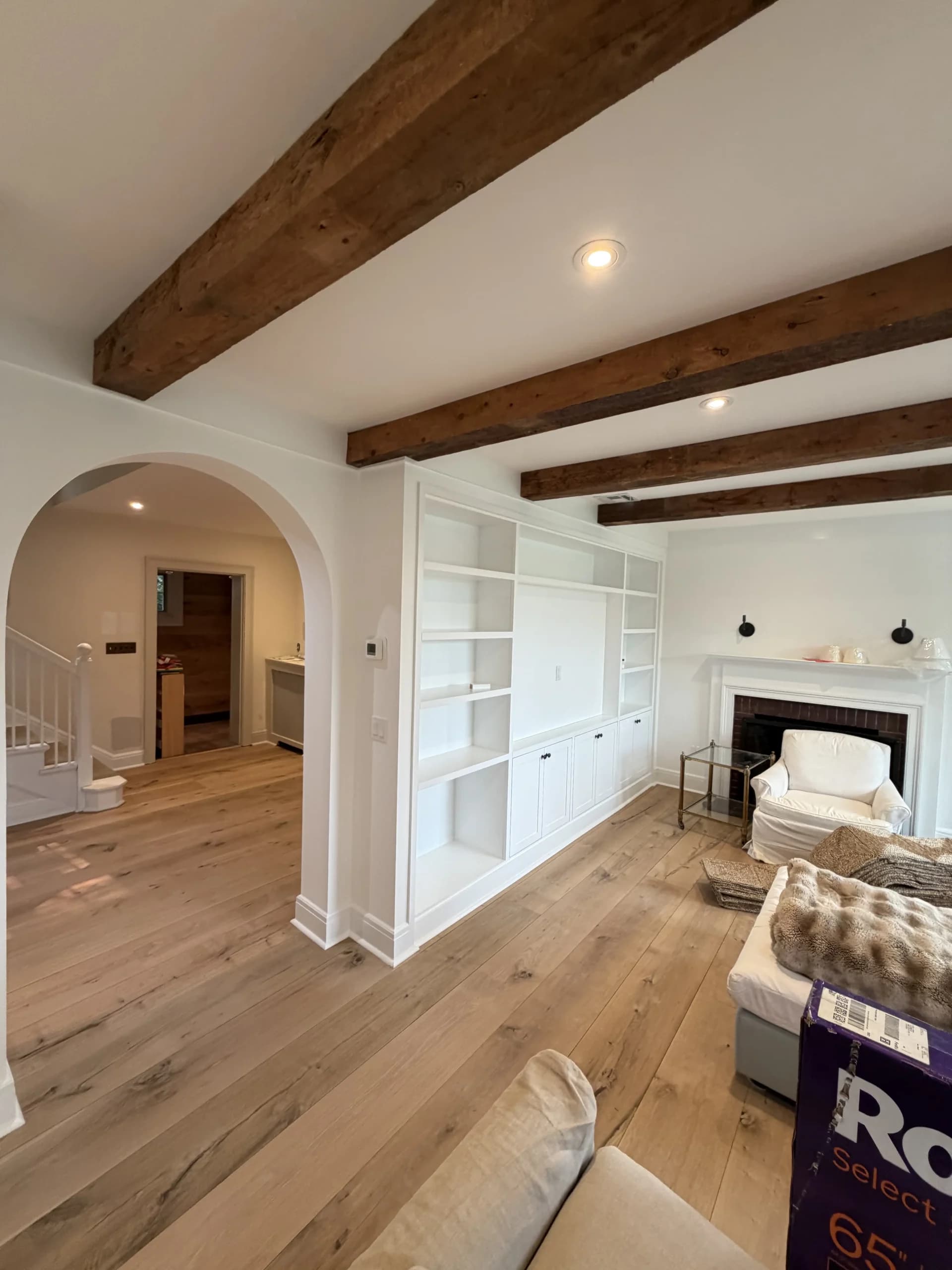 Open living room with exposed wood beams, an arched doorway and built-in shelving - home renovation by Greater Homes Solutions LLC