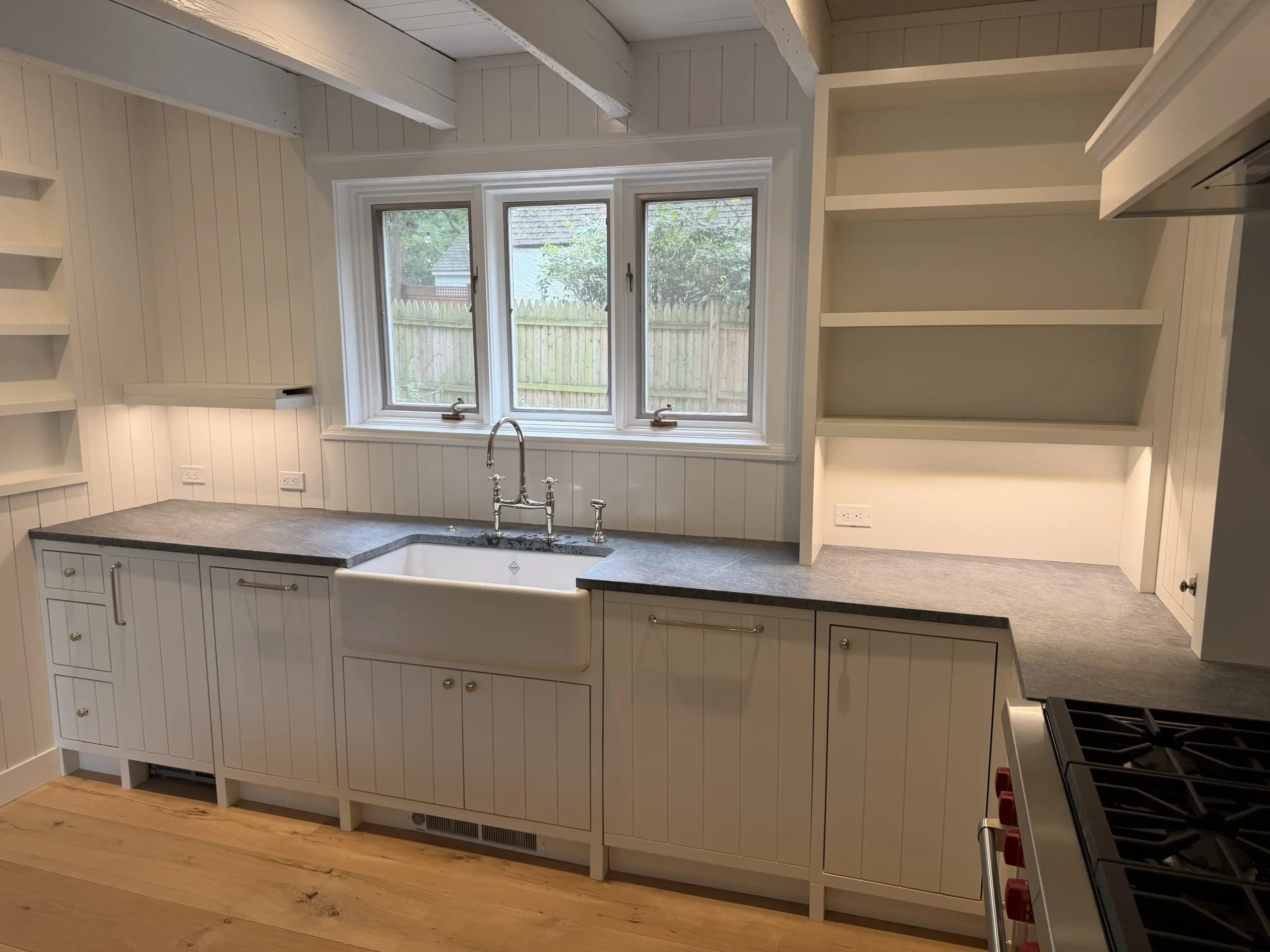 Farmhouse sink under a window with open shelving and white shaker cabinets - kitchen remodeling by Greater Homes Solutions LLC