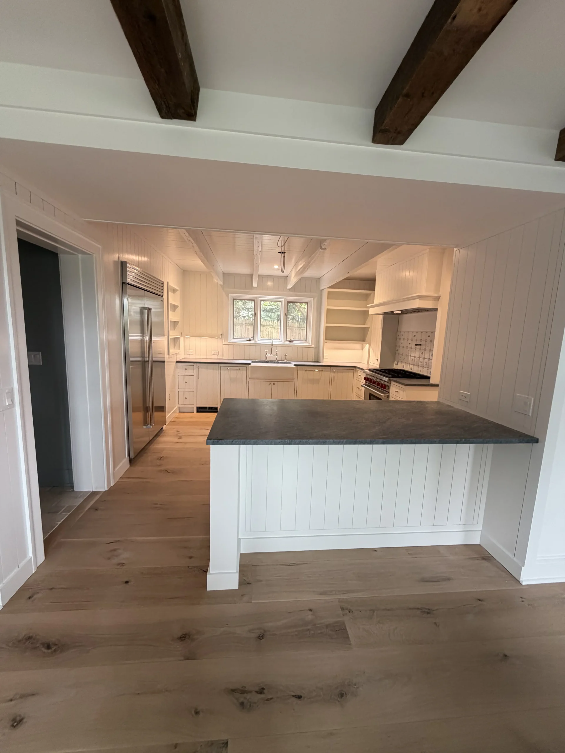 Kitchen with a slate-topped island under exposed beams, looking toward the range wall - kitchen remodeling by Greater Homes Solutions LLC
